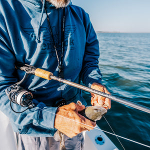 Man on a boat wearing a Fenwick blue Sweatshirts and fishing using as World Class Rod 