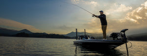Person fishing from a boat on a lake with mountains in the background