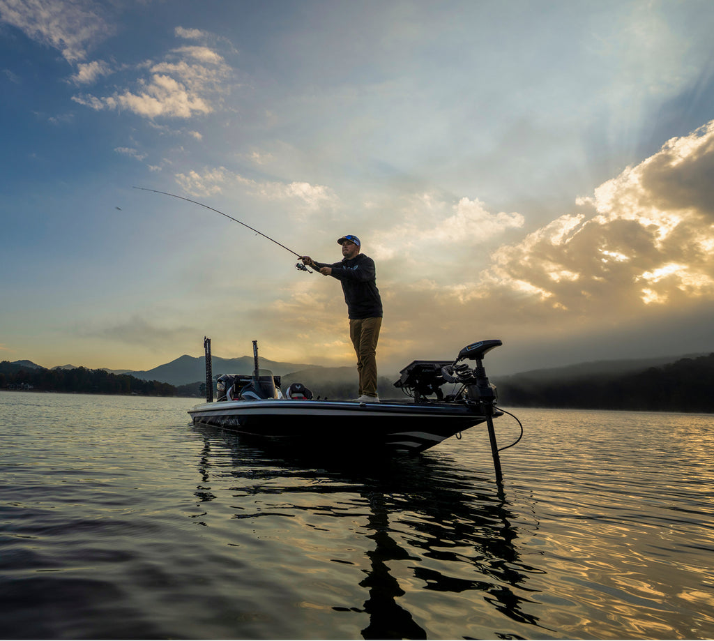 Man fishing from a boat on a lake with a sunset sky